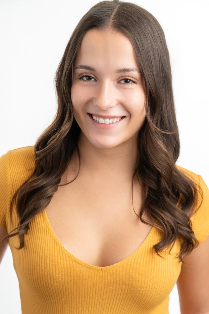 Professional headshot of Paris Mahan, founder of Mahan Marketing. She has long dark brown wavy hair and is wearing a mustard yellow ribbed top. She is smiling warmly at the camera against a clean white background.